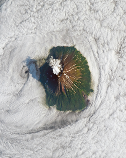 “Clouds surround the volcanic peak of Atlasov Island in the Russian Far East. Recorded volcanic activity here dates back to 1790 and continues today, evidenced the ash plumes in this Overview from August 2019. Atlasov, the northernmost of the Kuril Islands, is uninhabited and rises 7,674 feet (2,339 meters) above the Sea of Okhotsk.”
